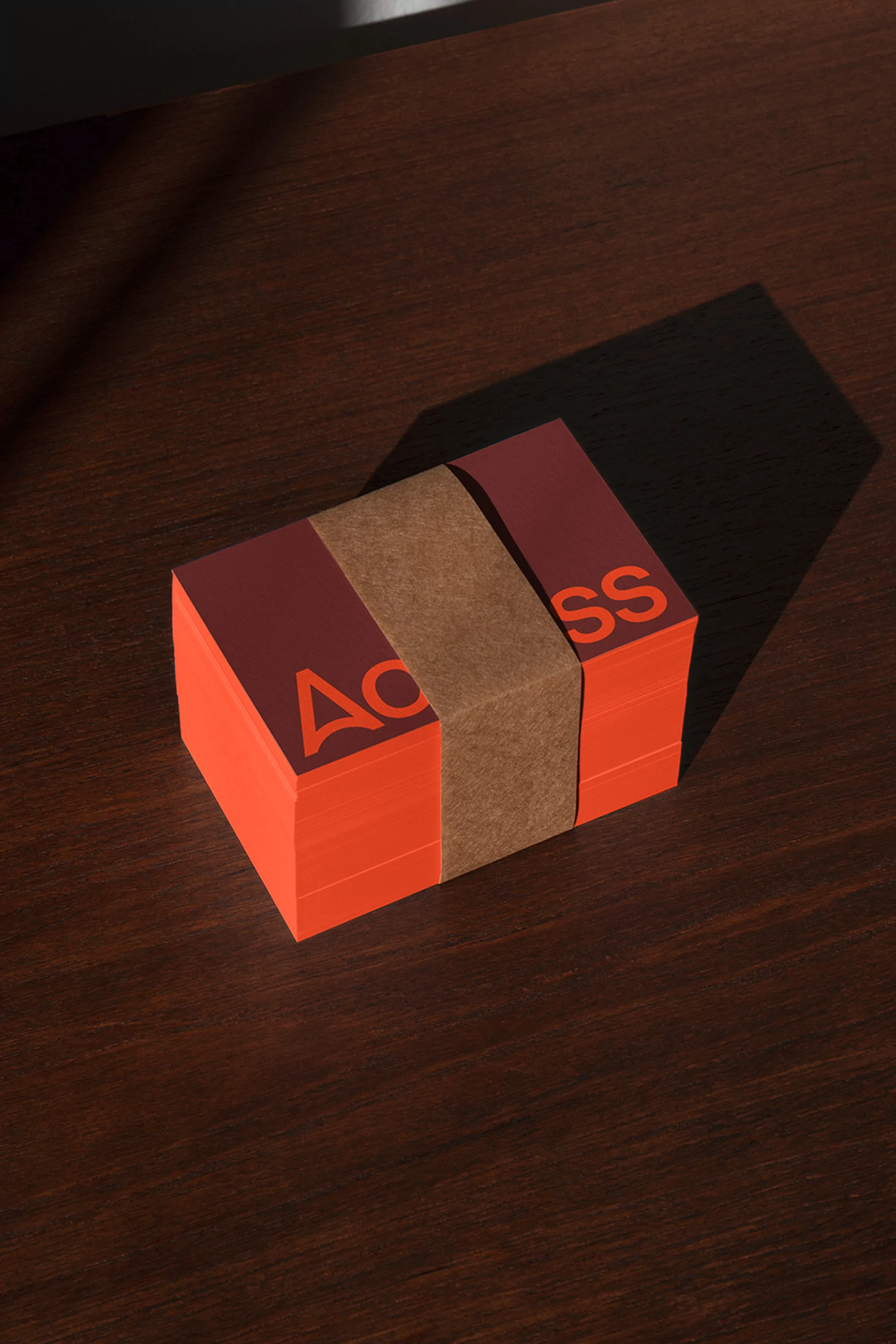 A stack of coral-colored cards with brown paper wrap and 'Access' printed on dark wood surface with shadow detail.