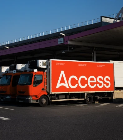 Two orange delivery trucks parked beneath a loading dock canopy with the company Access name in bold white letters on the side.