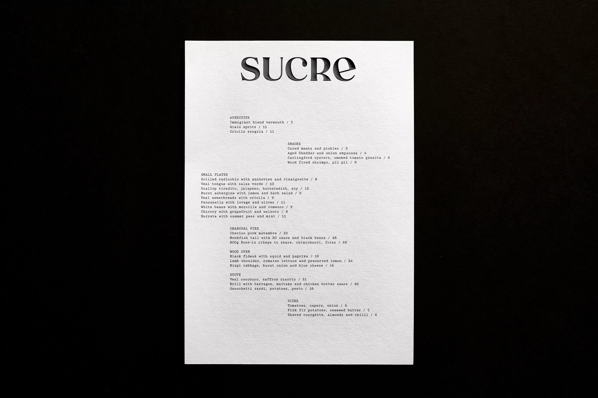 Menu from Sucre restaurant with appetizers, small plates, charcoal fire dishes, wood oven dishes, sides and nibbles on a white background.