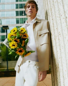 Male model in a tan jacket holding a bouquet of sunflowers against a stone wall