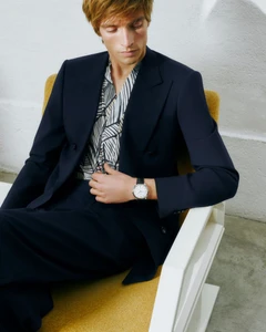 Male model seated in a white chair wearing a dark navy suit jacket and patterned shirt for Galeria Canalejas SS25