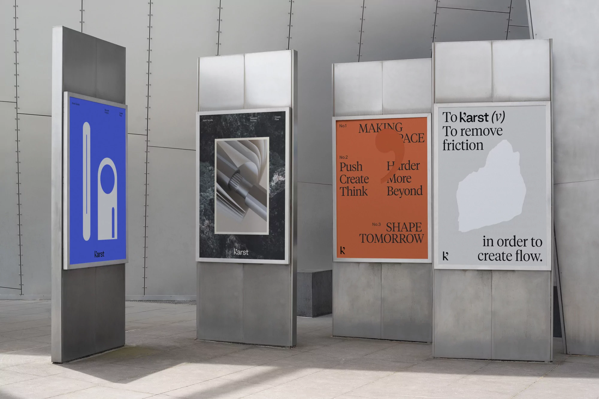 Four metal display stands feature graphic posters with geometric shapes and typography in an indoor setting, minimalist design.