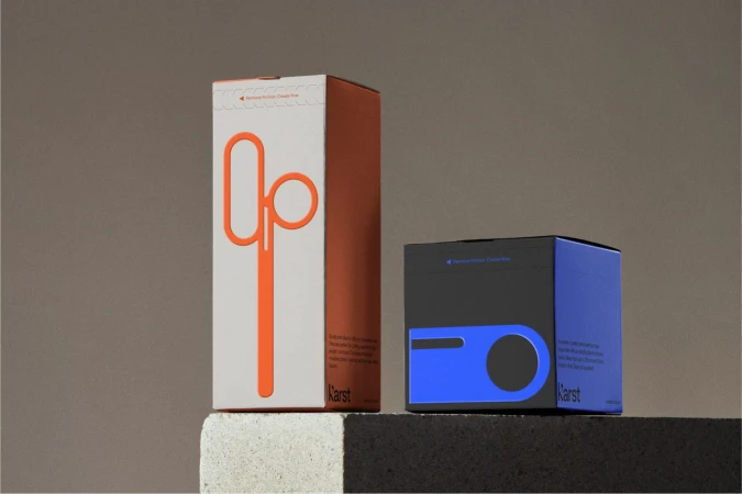 Two Karst stationery product boxes on a neutral surface show minimalist design, an orange paper up tool, and a blue planner box.