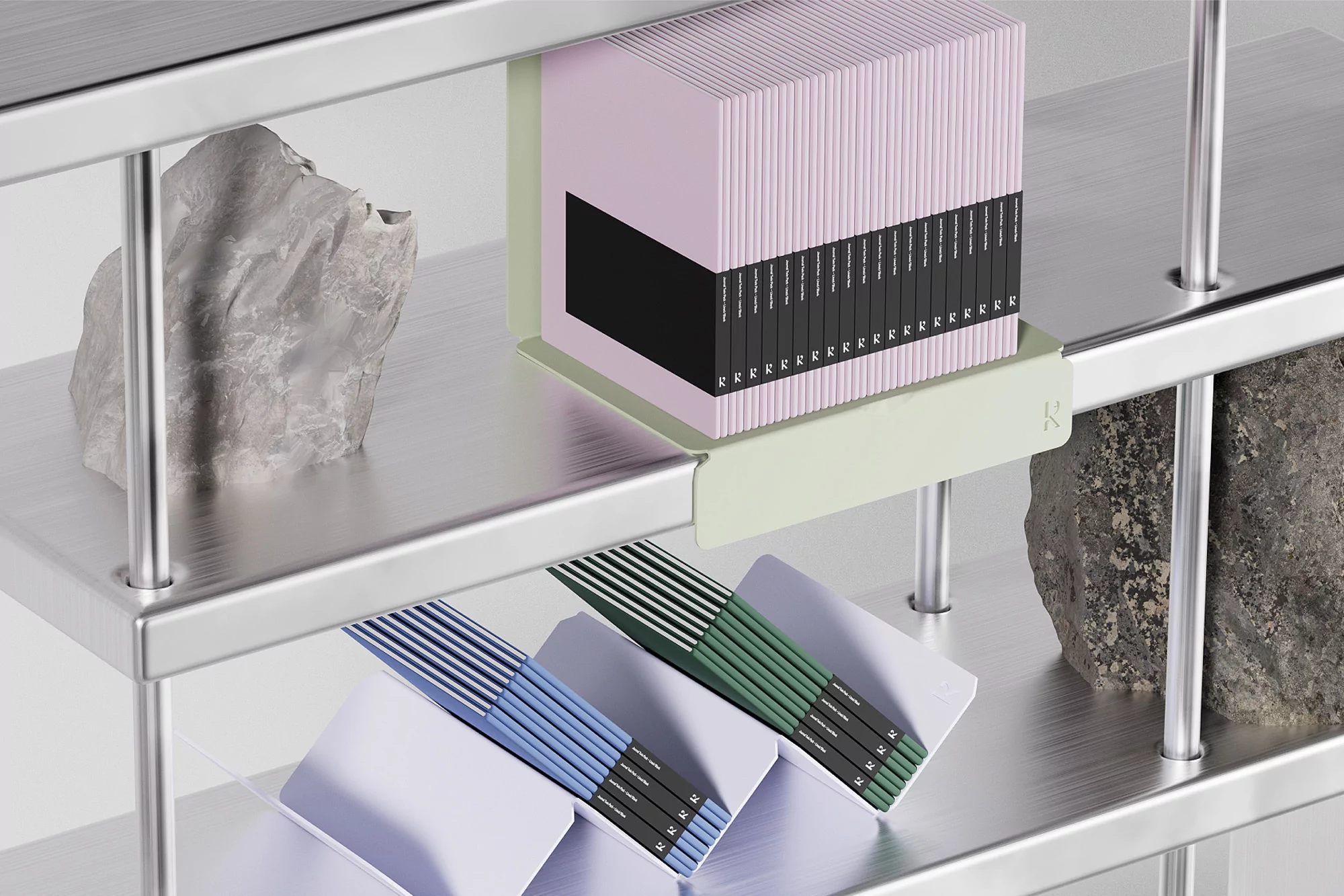 Close-up of a metallic shelf displaying stacks of books in pastel colors alongside decorative stones, set against a bright studio backdrop.