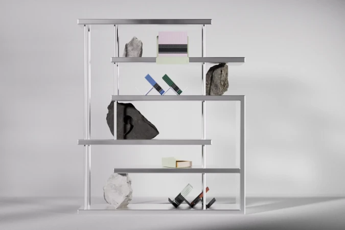 Minimalist interior design featuring a silver metal shelving unit with books, gemstones, and decorative objects against a plain white background.