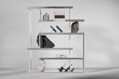 Modern metallic shelving unit displaying notebooks and raw stones on a neutral grey background.