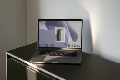 Laptop computer displaying website branding with the text remove friction on a dark cabinet against a white wall.