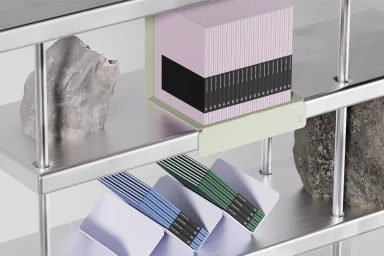 A set of pastel notebooks held by metal bookends on a sleek metallic shelving unit alongside textured stone pieces.