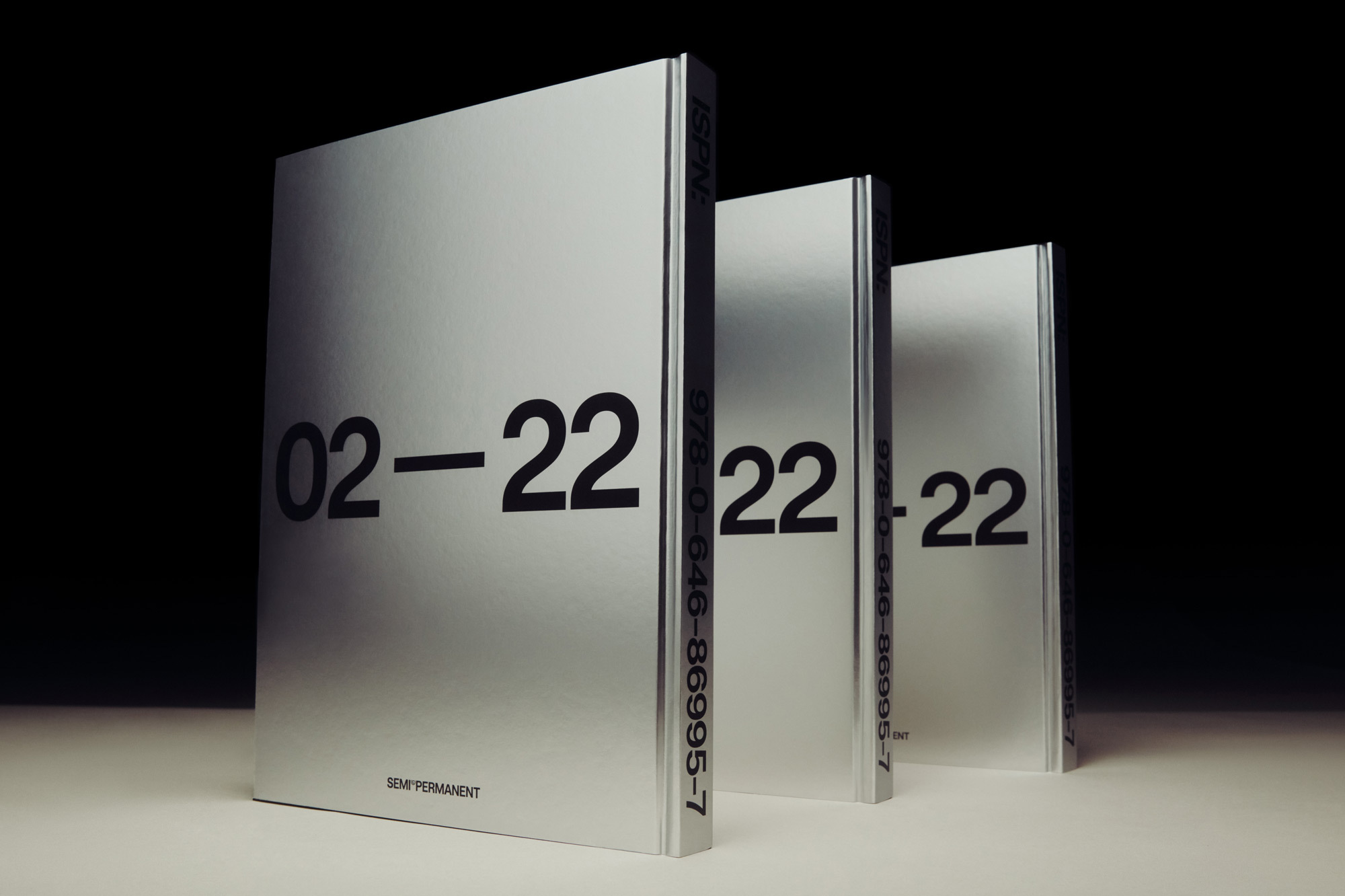 Three silver books stand in a row against a black background, displaying large, bold, black numbers '02-22' on their covers.