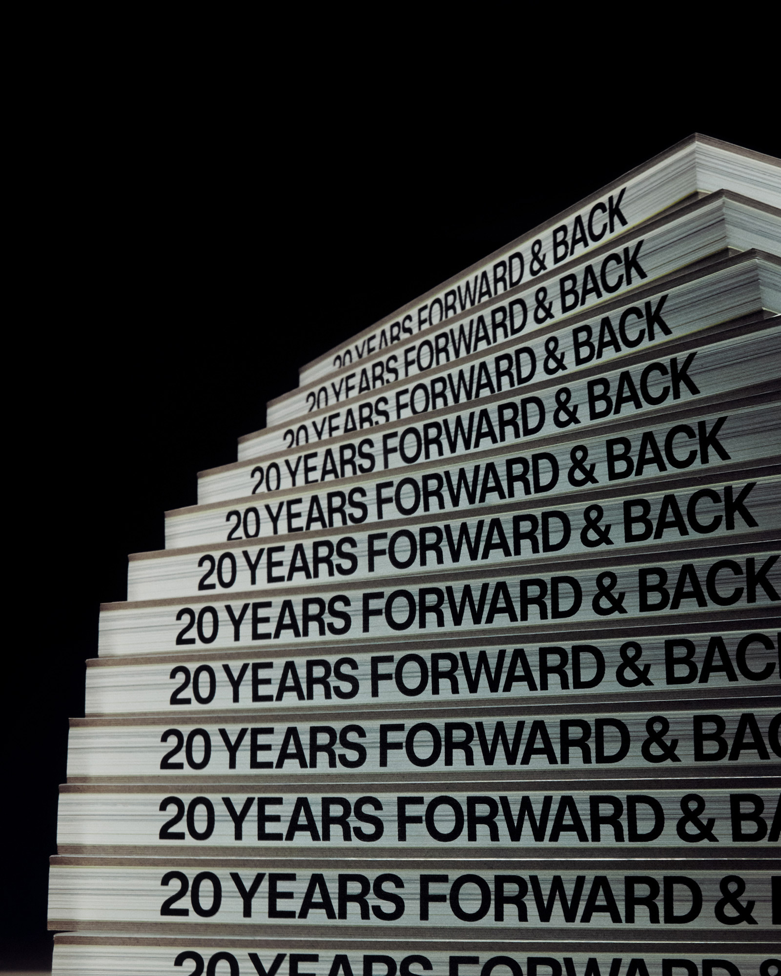Stack of books arranged like stairs against a black background, displaying repeating text '20 YEARS FORWARD & BACK' on the covers.