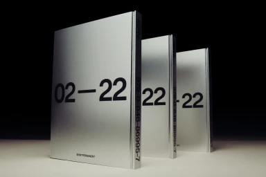 Three silver books with bold black typography arranged in a row on a light surface against a dark background.