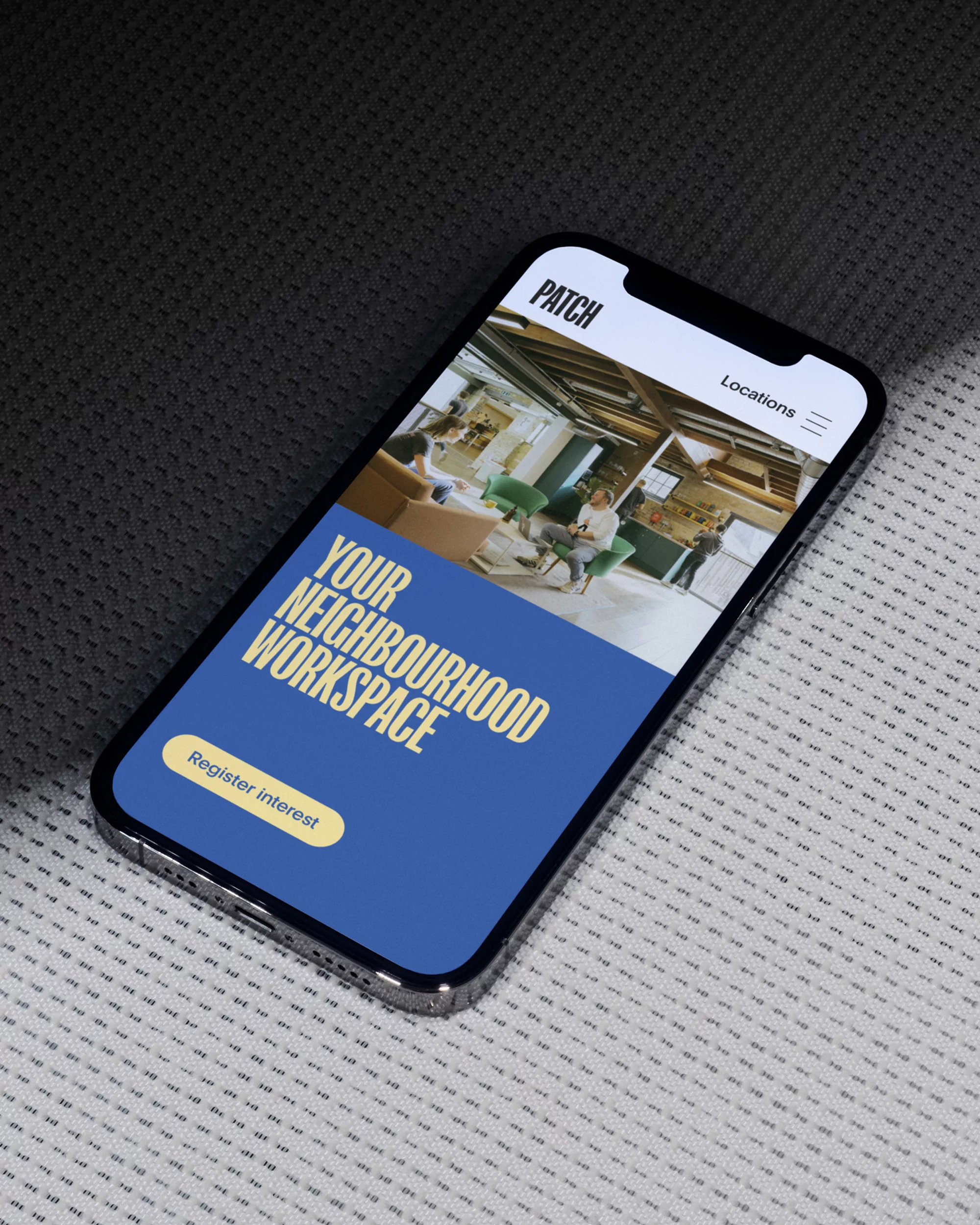 Mobile phone displays coworking space ad; advert shows a modern workspace with blue background & text reading 'Your Neighborhood Workspace'.