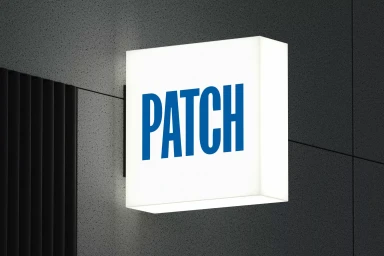 Illuminated square box sign displaying the blue Patch brand logo mounted on a dark textured wall