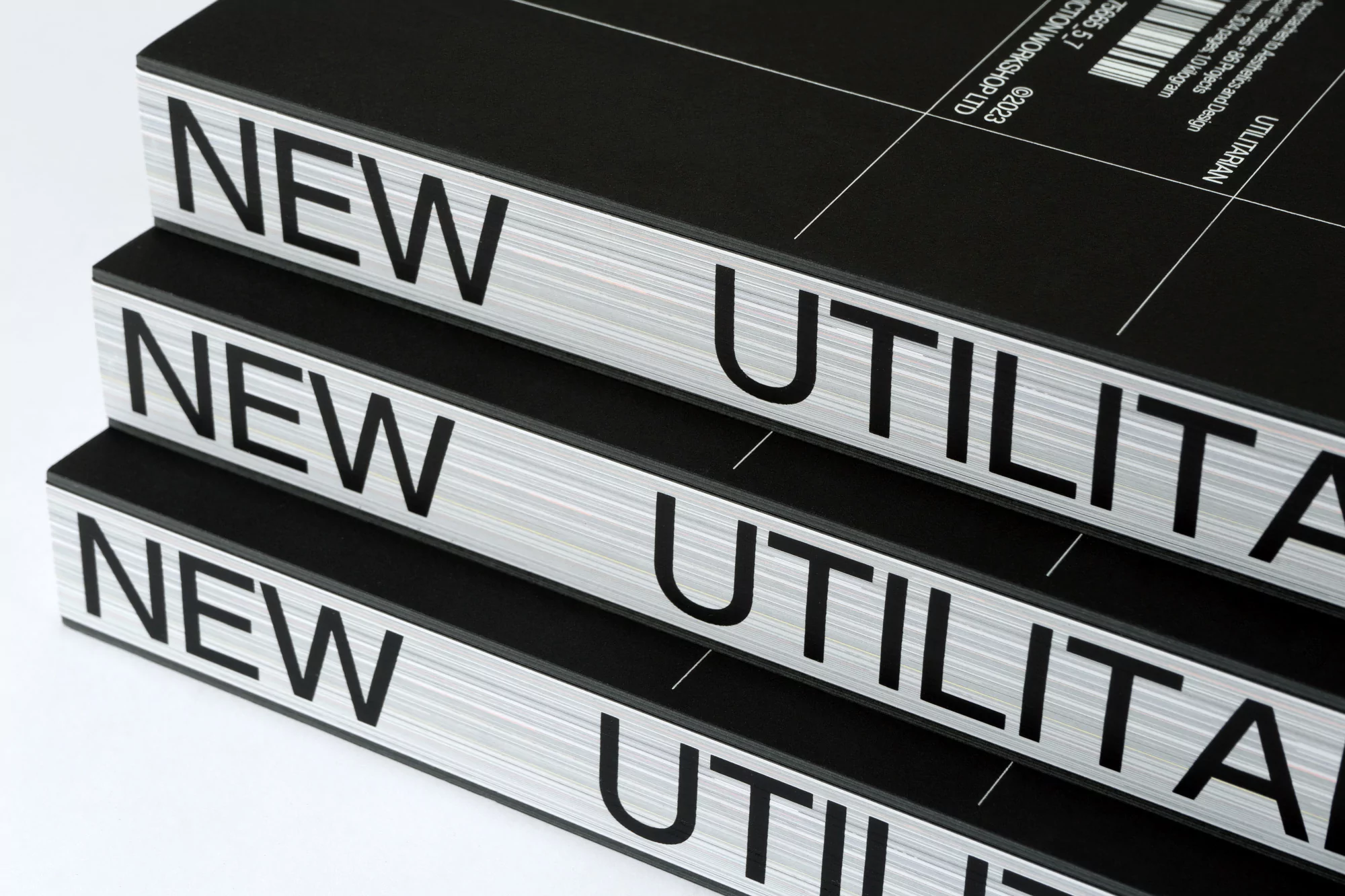 Close-up of three stacked books with the words 'New Utilitarian' in black text on a silver band against a black background.
