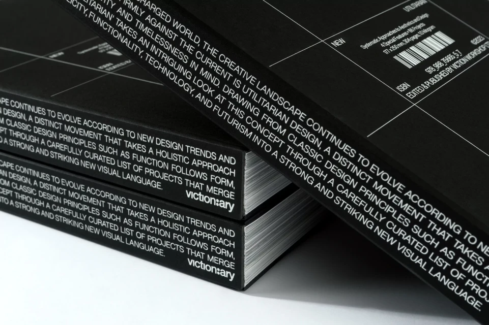 Two black books titled "victionary" stacked on a white surface, with text describing design principles and movements visible.
