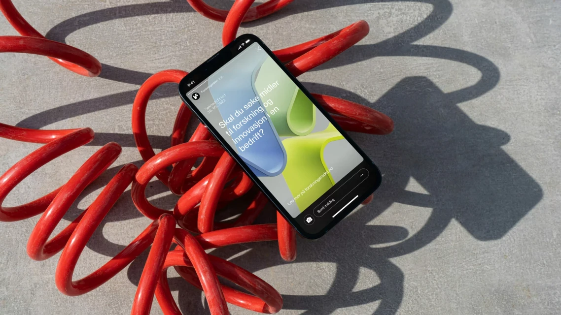 A smartphone displaying an abstract design rests on a grey surface surrounded by a vibrant red coiled cable, casting soft shadows.