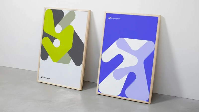 Two framed abstract graphic design posters leaning against a plain wall on a concrete floor.