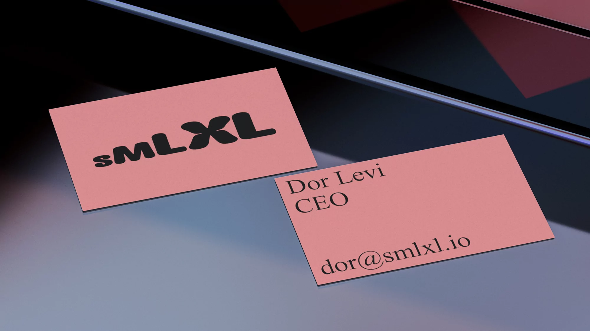 Close-up of two pink business cards on a glossy surface, one with 'sMLXL' logo, the other with contact details.