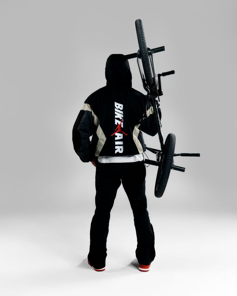 Man in jacket with bike over shoulder stands in a studio. Sports and fashion are merged in clean product-style shot.