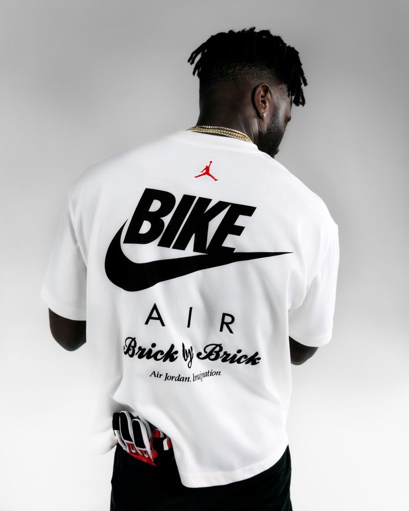 Back view of an adult male in a white t-shirt with black Nike and Air Jordan logo graphics against a plain white backdrop.