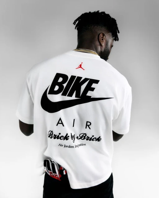 Back view of an adult male in a white t-shirt with black Nike and Air Jordan logo graphics against a plain white backdrop.