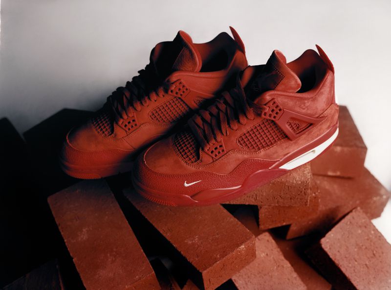 Two red Nike Air Jordan 4 Retro sneakers displayed on a pile of red bricks, photographed in a studio with side lighting.