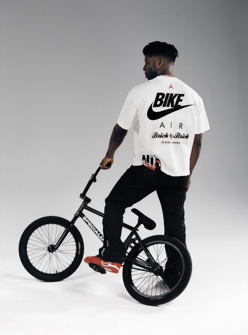 A man on a BMX bicycle wears a t-shirt with 'Bike Air' printed on the back in a studio with even lighting and a neutral backdrop.
