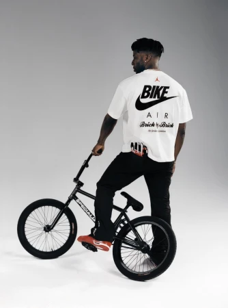 A man on a BMX bicycle wears a t-shirt with 'Bike Air' printed on the back in a studio with even lighting and a neutral backdrop.