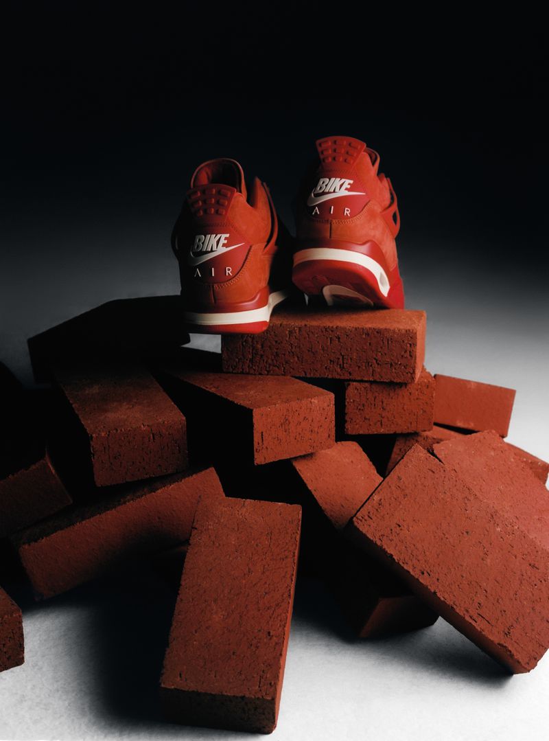 Two red Nike Air Flight Huarache sneakers are positioned on top of a stack of red bricks in a studio setting, back view.