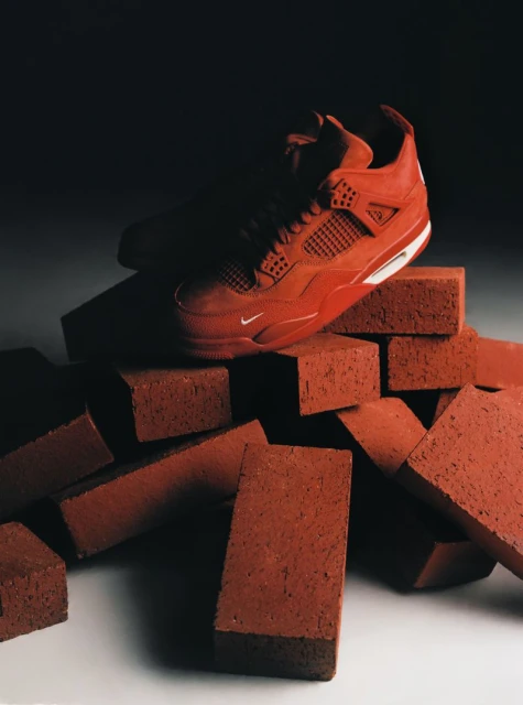 Red basketball shoe on a pile of red bricks in a studio with soft lighting. Athletic footwear product photography for social media.