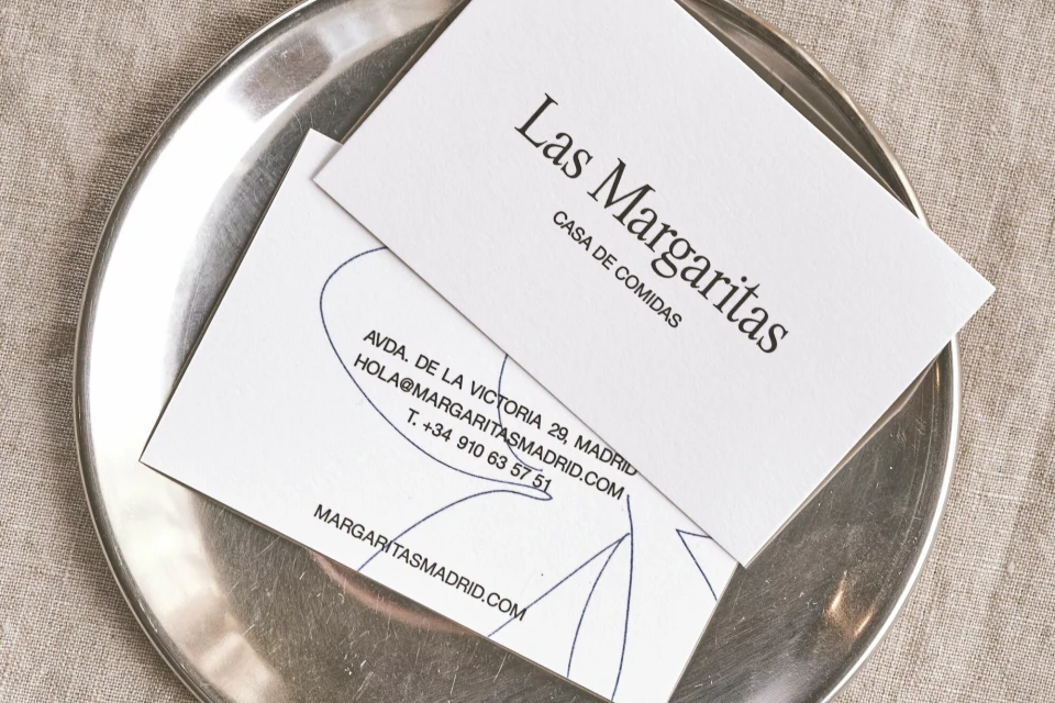 Close-up shot of two white business cards with black text on a shiny silver plate, with a neutral, textured fabric in the background.