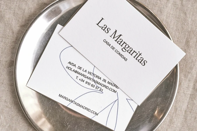 Close-up shot of two white business cards with black text on a shiny silver plate, with a neutral, textured fabric in the background.