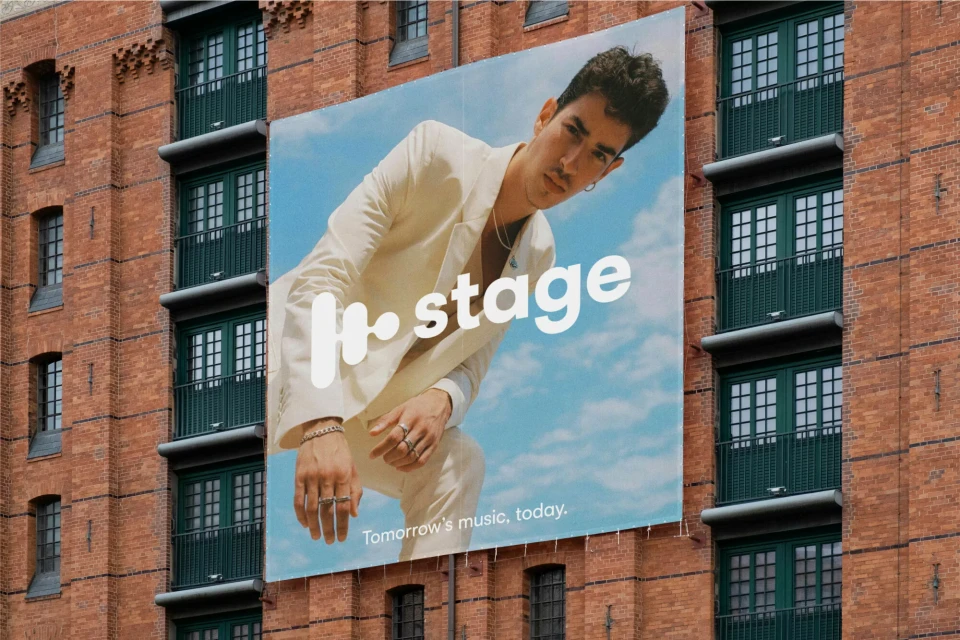 Outdoor advertisement for music featuring a young adult male in a white suit against a blue sky, displayed on a brick building.
