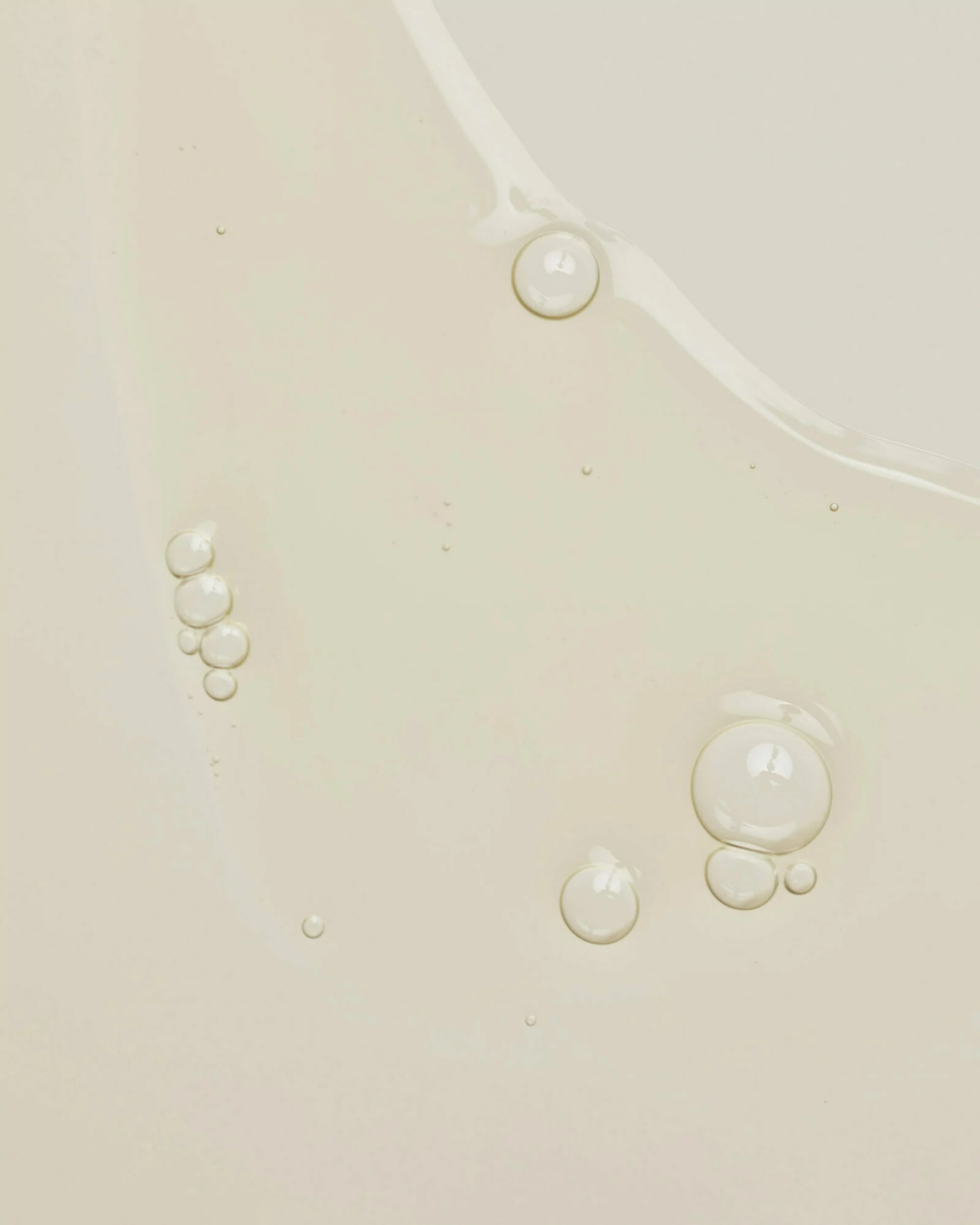Close-up of cosmetic serum with varying sized clear bubbles, light olive-beige color, and a reflective surface.