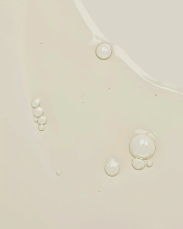 Close-up of cosmetic serum with varying sized clear bubbles, light olive-beige color, and a reflective surface.