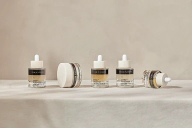 Five skincare bottles and jars from Team Dr Joseph arranged in a row on a neutral surface against a matching backdrop.