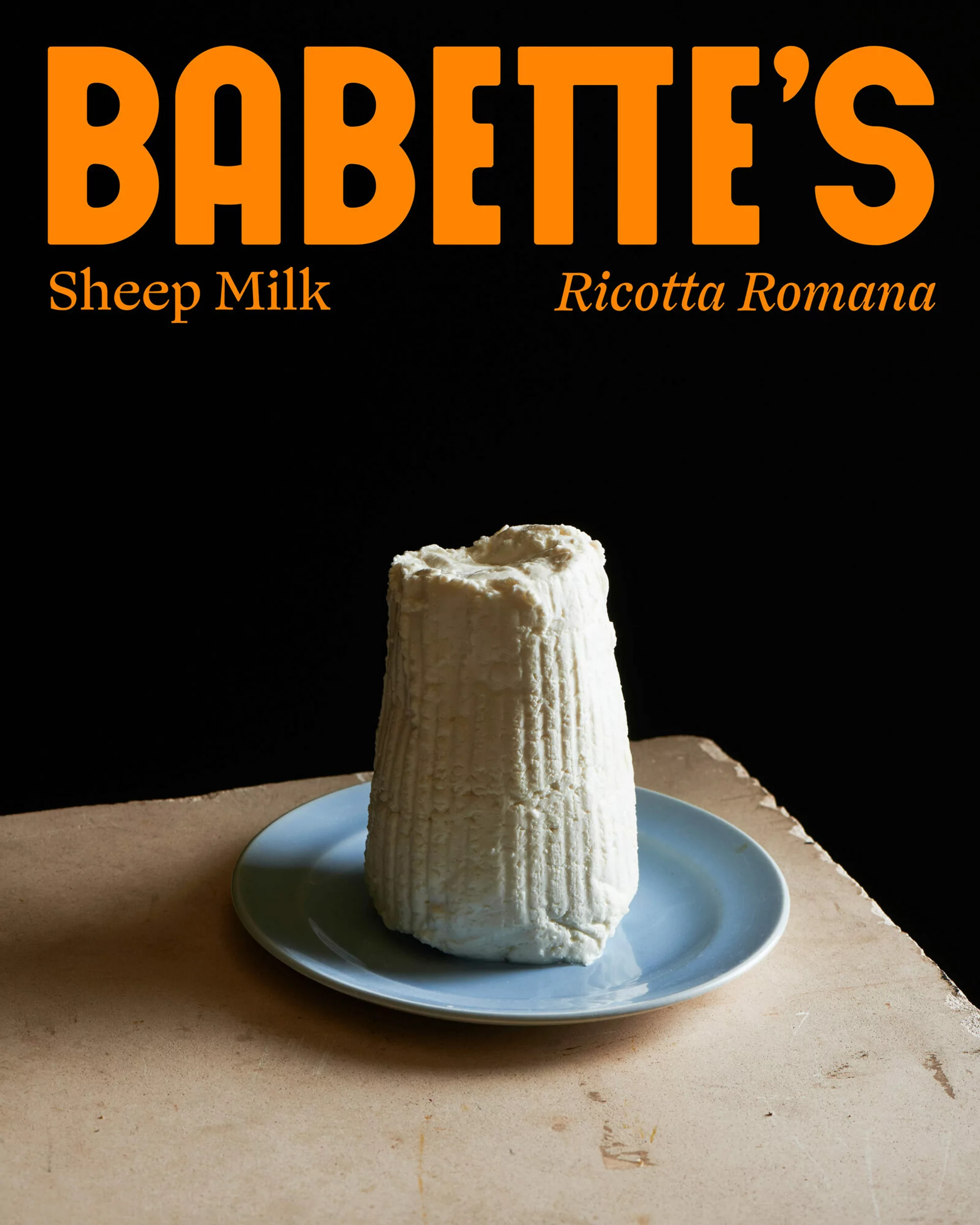 Close-up studio shot of fresh ricotta cheese on a blue plate against a dark backdrop with food typography in shades of orange.
