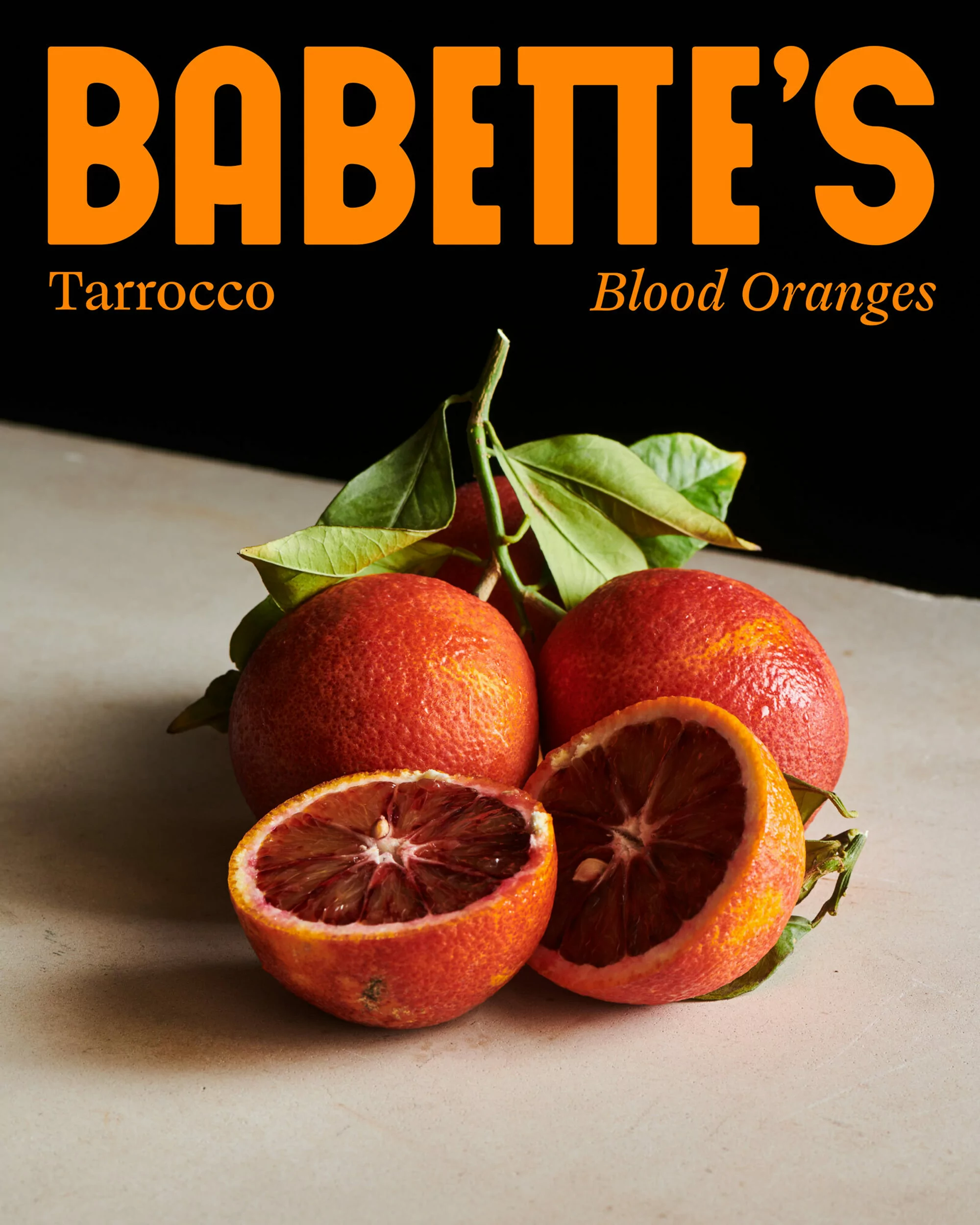 Vibrant still life featuring a group of ripe blood oranges, with one cut open, showcasing their deep red flesh and juice, resting on a table.