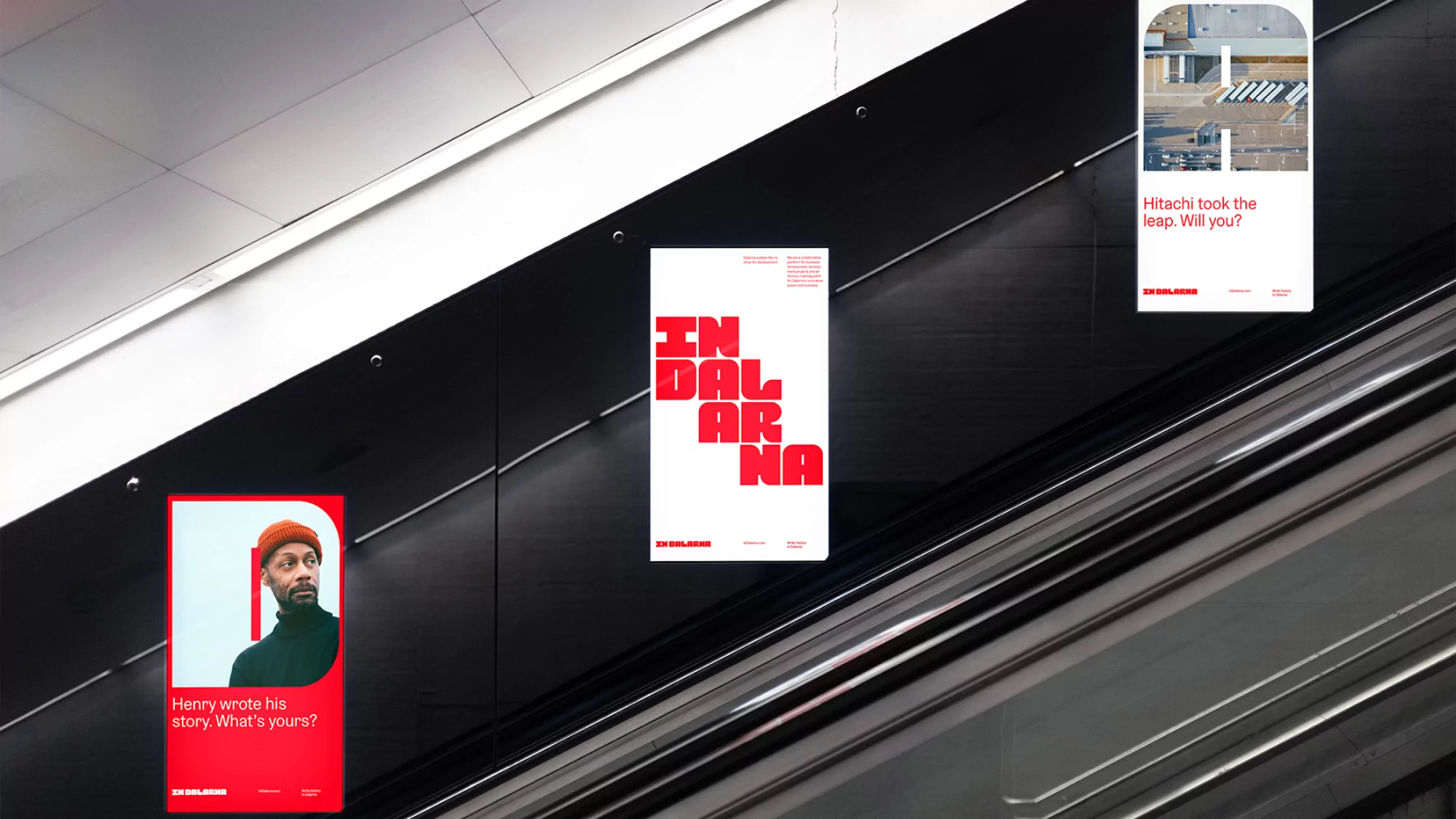A view from an escalator looking at three advertising posters on a dark wall, one with a man's portrait.