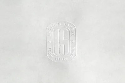 Embossed logo on light grey paper texture featuring a rectangular stamp with rounded corners and centered typography.