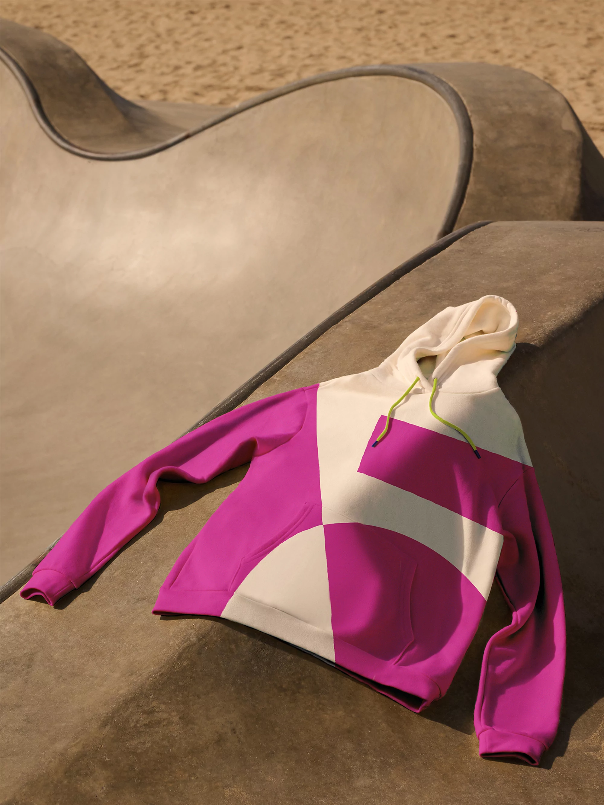 Hoodie sweatshirt with magenta and cream color blocking on a concrete skatepark structure in a medium shot on a sunny day.
