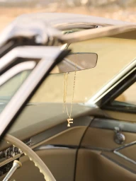 Gold letter necklace hanging from the rearview mirror inside a vintage car interior