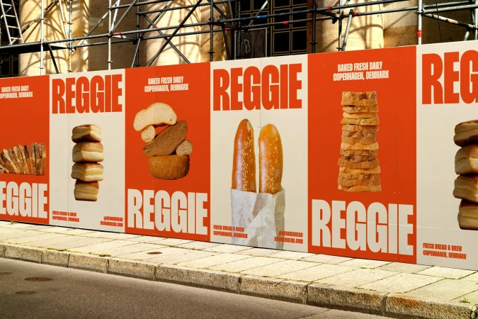 Street-level view of advertising hoarding with 'Reggie' bread ads featuring stacked bread loaves on an orange and white background.