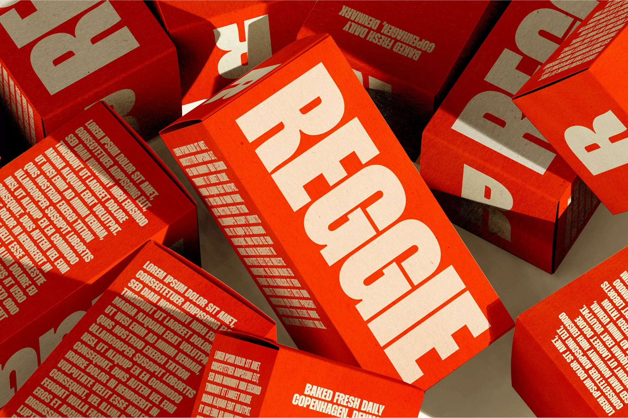 Multiple red and white product boxes stacked randomly, displaying the brand name 'REGGIE' and marketing text against a neutral backdrop.