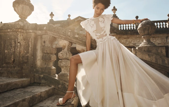 Model Lineisy Montero in a white lace dress posing on a stone staircase for Zimmermann Spring RTW.