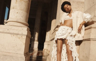 Model Lineisy Montero leaning against neoclassical columns in a white lace skirt and jacket for Zimmermann Spring RTW