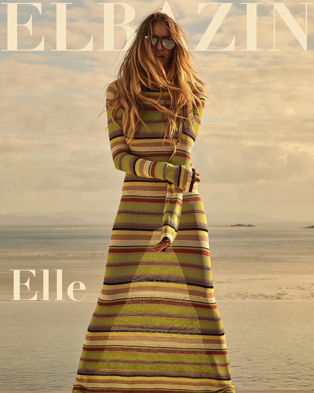 Woman in a striped maxi dress and sunglasses standing outdoors near water for Elbazin Magazine