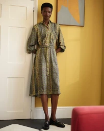 Model standing against a white paneled door wearing a patterned midi shirt dress and dark loafers in an interior room