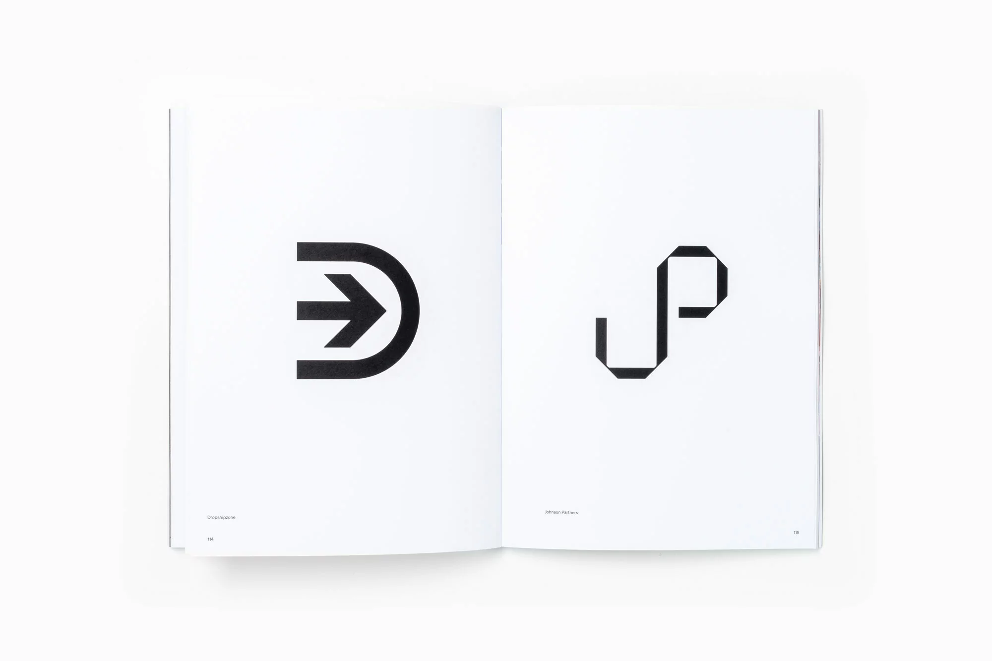 Open book displaying minimalist black and white graphic designs featuring an arrow and the letters 'JP' on contrasting pages.
