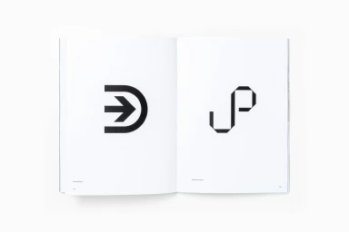 Open book displaying minimalist black graphic identity marks on clean white pages against a plain background